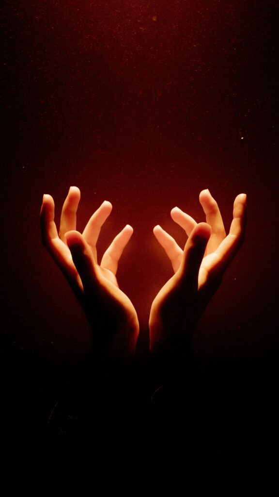 Illuminated hands reaching upward in a dark, warm setting, creating a sense of wonder.